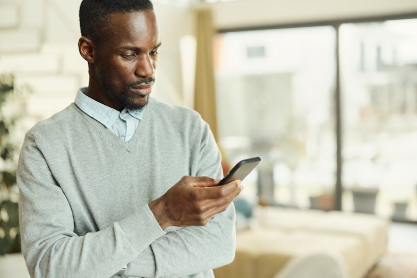 Young black man reading a text message on mobile phone at home. Copy space.