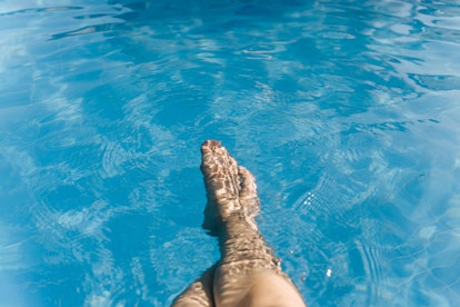 Female legs in the blue transparent water of the pool. Point of view.