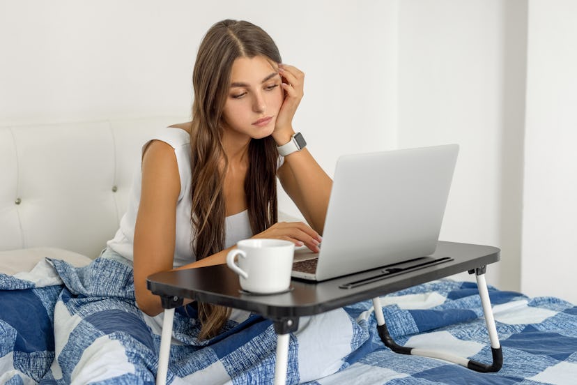 Girl lying in bed at home and watching movies during lazy weekend