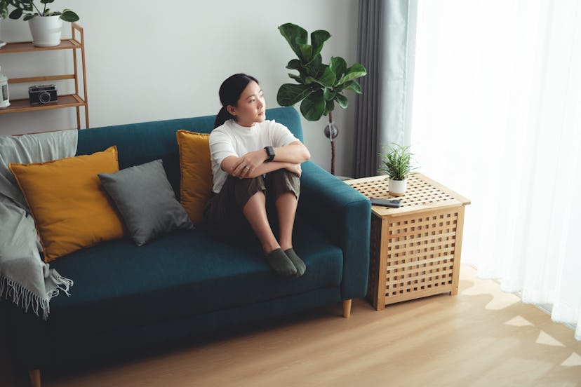 Asian woman feeling lonely thinking about problem sitting embracing knees on sofa in living room at ...