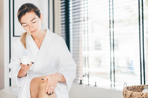 Woman takes care of her skin.  Woman applies cream to her legs in the bathroom.