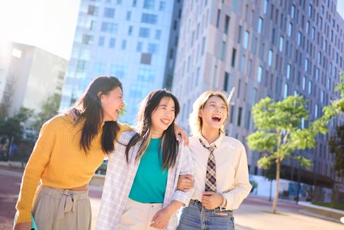 Three female Chinese friends having fun together outdoors in the city, embracing each other, talking...