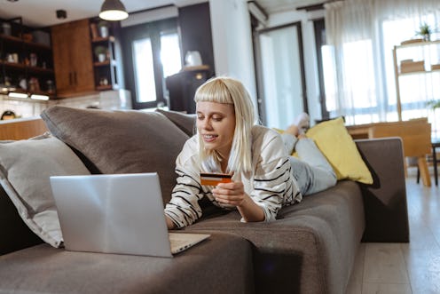 Shot of a beautiful young woman using her laptop and credit card while relaxing on a sofa at home