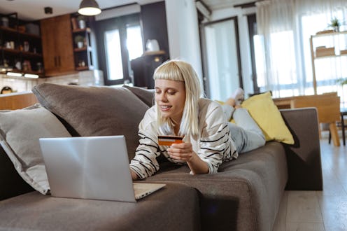 Shot of a beautiful young woman using her laptop and credit card while relaxing on a sofa at home