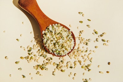 Wooden spoon with purified and ground hemp seeds on beige background. Hemp food supplements. Flat la...