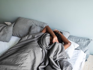 Depressed young adult black woman with headache lying in bed and hiding under blanket