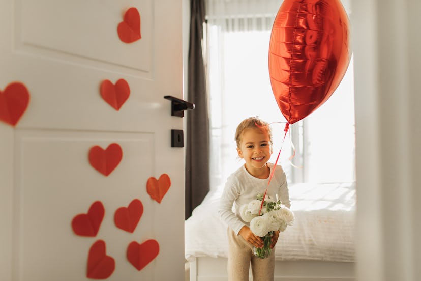 Little cute girl makes a surprise for her mother and sticks handmade red paper hearts on the door. S...