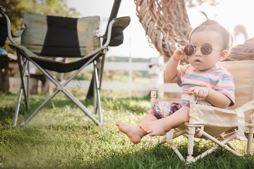 The cute baby girl wears sunglasses enjoying and funny sitting on the chair in the park on the sunsh...