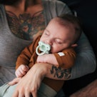 Young female with tatoos holding her baby in hera arms. Baby is sleeping.