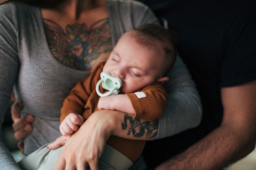 Young female with tatoos holding her baby in hera arms. Baby is sleeping.