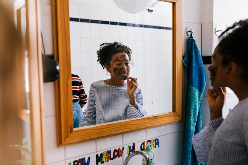 Tween girl applying facial mask while looking into a bathroom mirror, in a story about kid-safe skin...