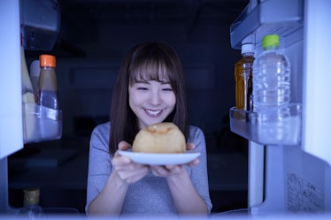 Jeune femme japonaise mangeant une collation de nuit dans le réfrigérateur