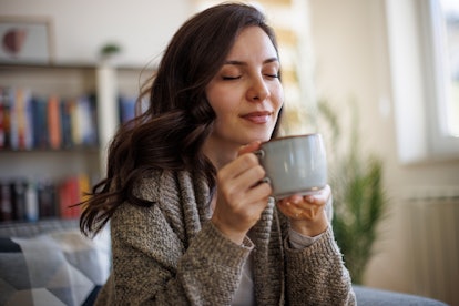 Young smiling woman enjoying in smell of fresh coffee at home