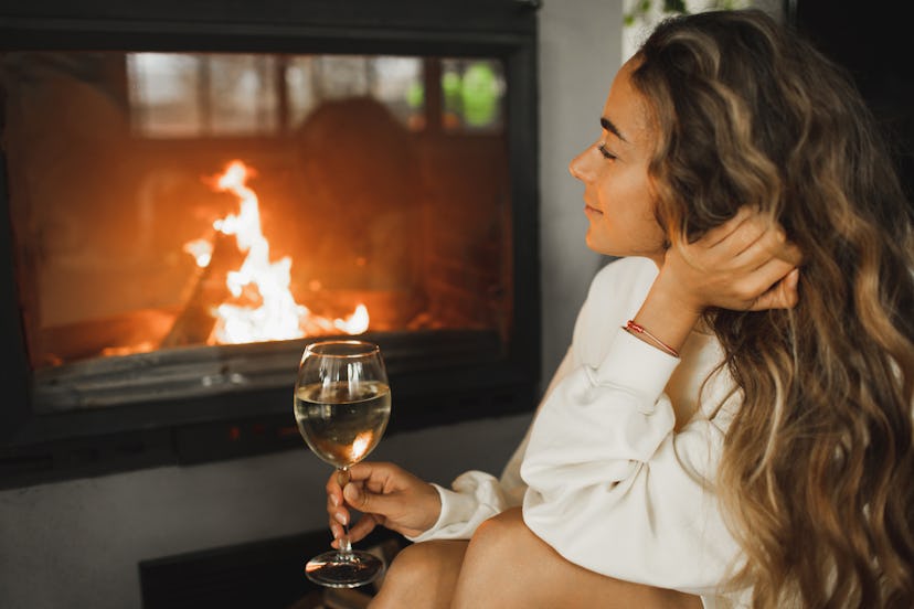 Lady resting alone on fireside and enjoying cold wine. Wellbeing and pleasure, leisure in evening. B...