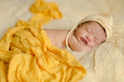 Newborn girl sleeping comfortably on a hat, blanket and yellow background. Selective focus