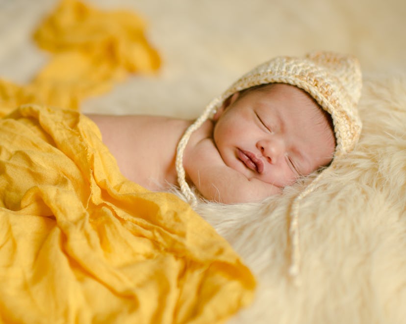 Newborn girl sleeping comfortably on a hat, blanket and yellow background. Selective focus