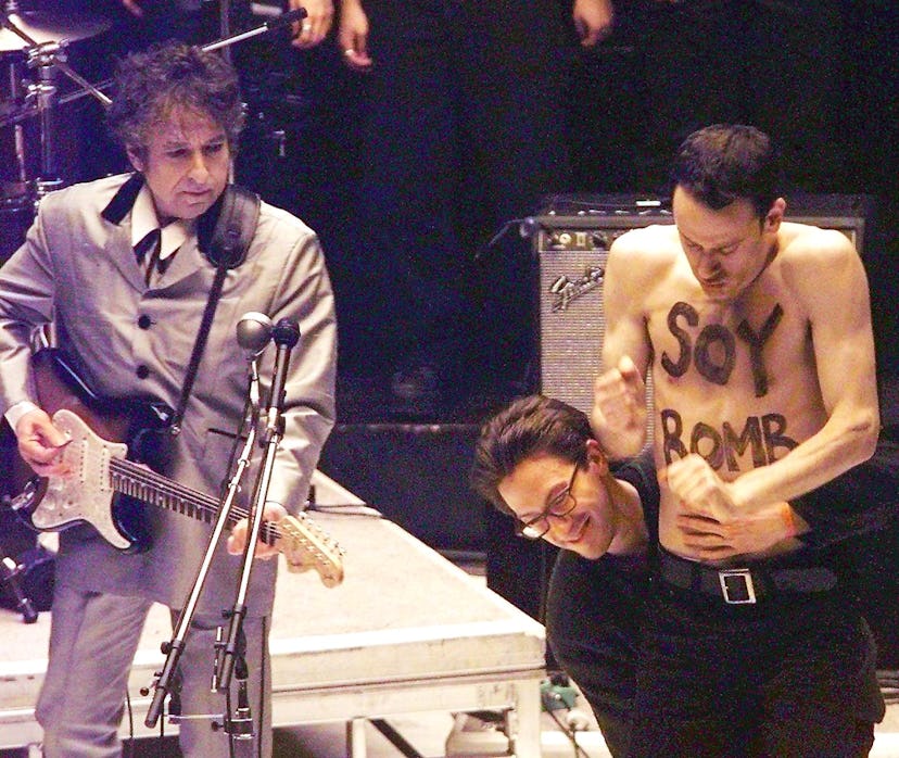 A demonstrator with "Soy Bomb" painted on his chest is removed from the stage as Bob Dylan performs ...