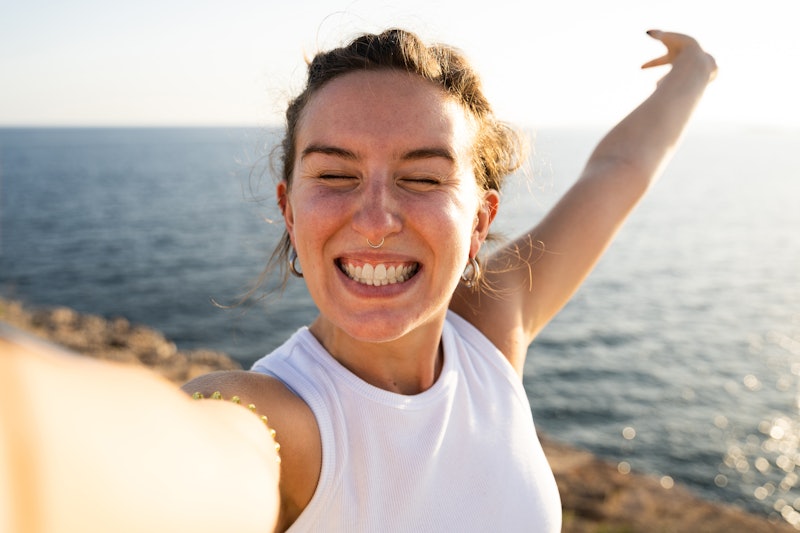 A happy woman because she is enjoying her summer vacation. She is taking a selfie with her phone at ...