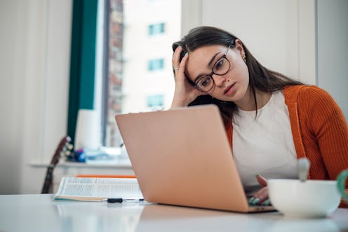 Front view of a young woman wearing casual clothing sitting at a desk using a laptop to study, she i...