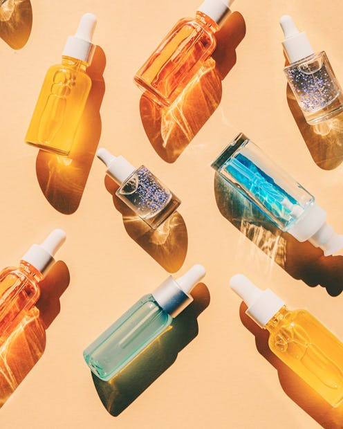 Assorted glass bottles with cosmetic liquids, serum or gel. Vibrant trendy background of cosmetic pr...