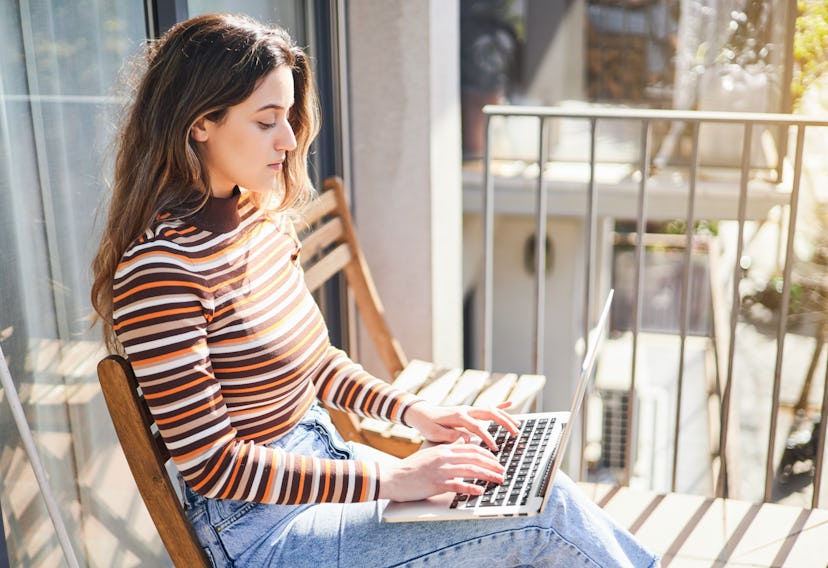 Portrait of a beautiful young woman working on her laptop from the terrace of her house.