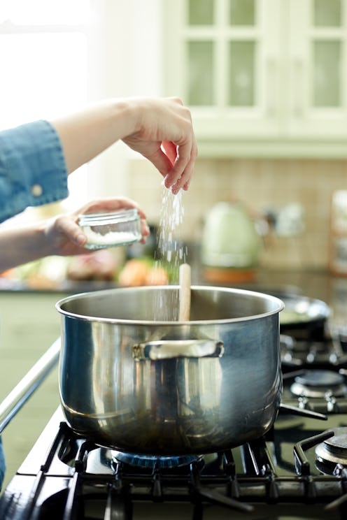 Close-up cropped image of woman adding pinch of salt in cooking pan. Utensil is placed on stove. Clo...