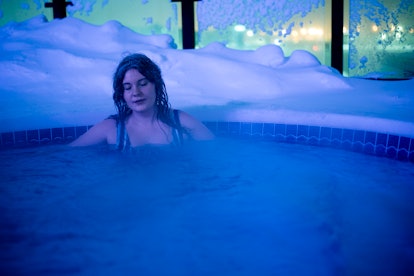 Female tourist in her 20's soaks in a hot tub rimmed by sow on a fridig cold evening outdoors, Calga...