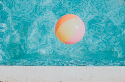 Simple background image of a multicoloured pink, orange and yellow beach ball floating in an outdoor...