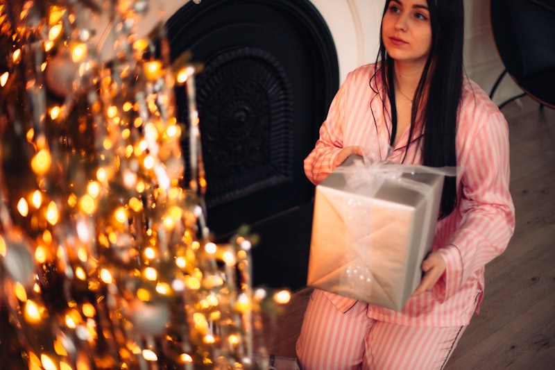 Young woman holding Christmas present while sitting by Christmas tree at home