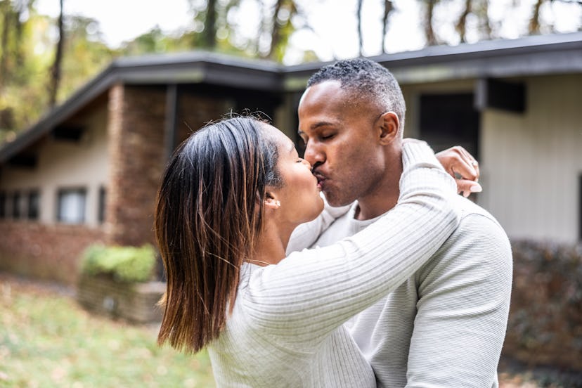 Married couple kissing in front of suburban home