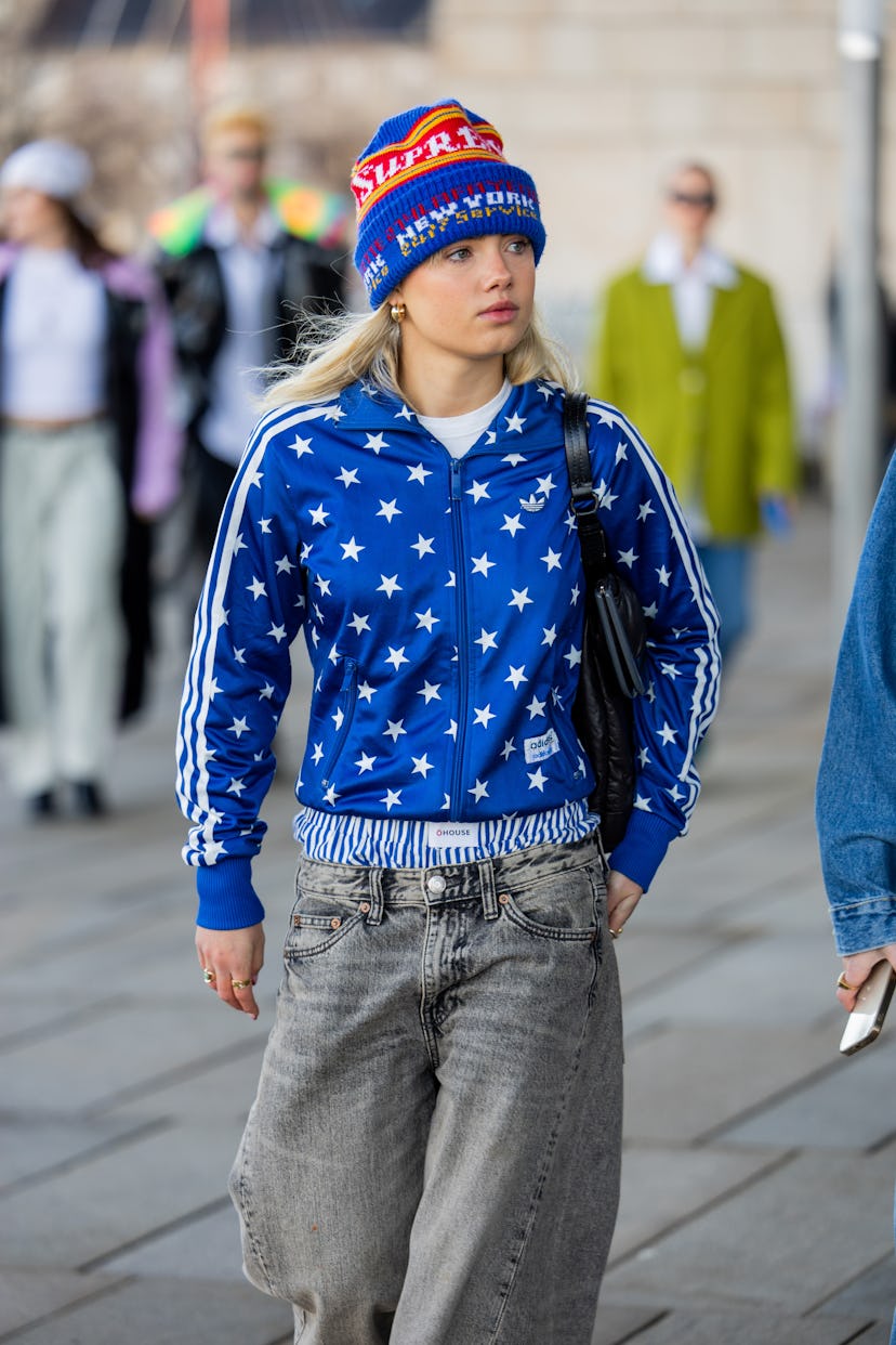 COPENHAGEN, DENMARK - JANUARY 31: A guest wears blue beanie, jacket with star print, grey denim jean...