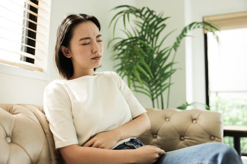 Young Asian woman with stomach ache at home