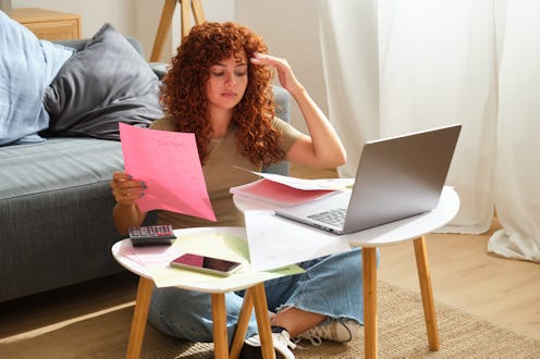 Young redhead freelancer woman feeling stressed working from home having financial problems doing ta...