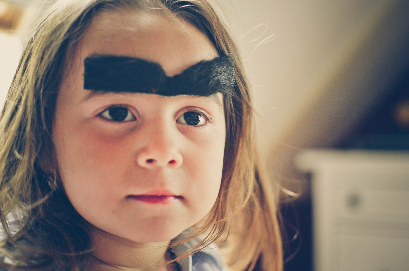 A young girl wearing a silly large bushy black unibrow costume.