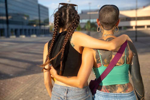 Two young women walking arm in arm embracing, rear view