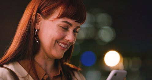 Woman, smartphone and bokeh with smile, communication and texting at night in city. Journalist, cell...