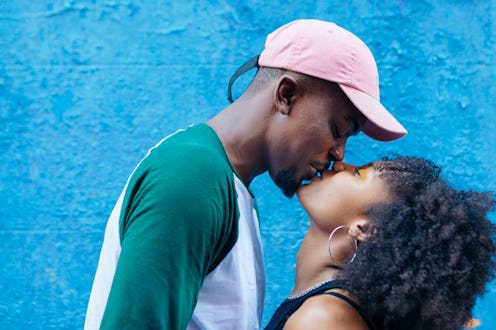 Horizontal side view of hispanic couple with afro hairstyle kissing with love outdoors. People diver...