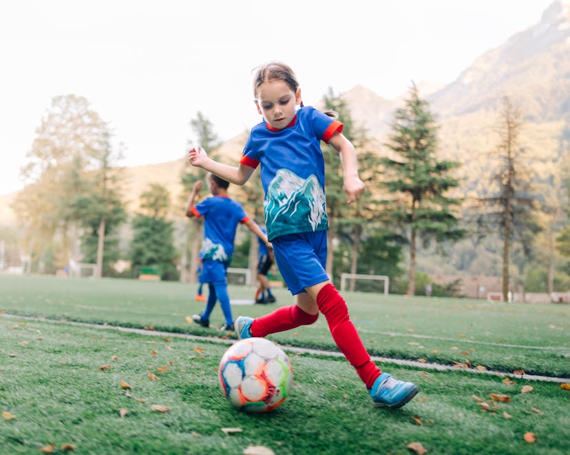 Young girl child soccer player exercises with a ball and running on the soccer field, football