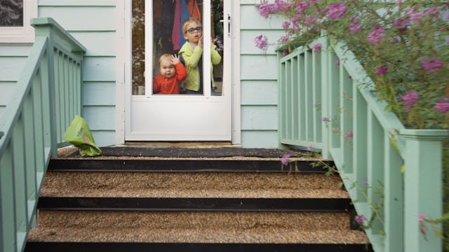 Two adorable little brothers pressing their faces against the window of their front door at home