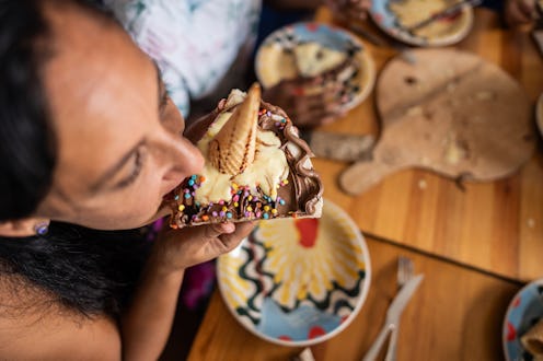 Mature woman eating a slice of a sweet pizza with ice cream cone at restaurant
