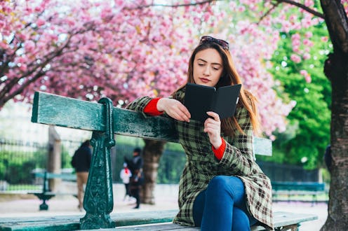 Beautiful woman sitting at bench and reading an e-book