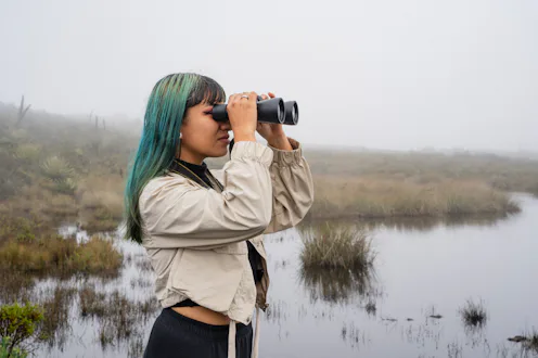 Latin and young woman with binoculars at the lake, searching for wild birds
