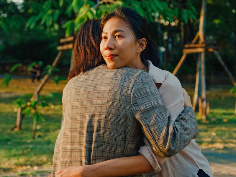 Closeup two young Asian women sharing a supportive embrace in a public park during mental health awa...