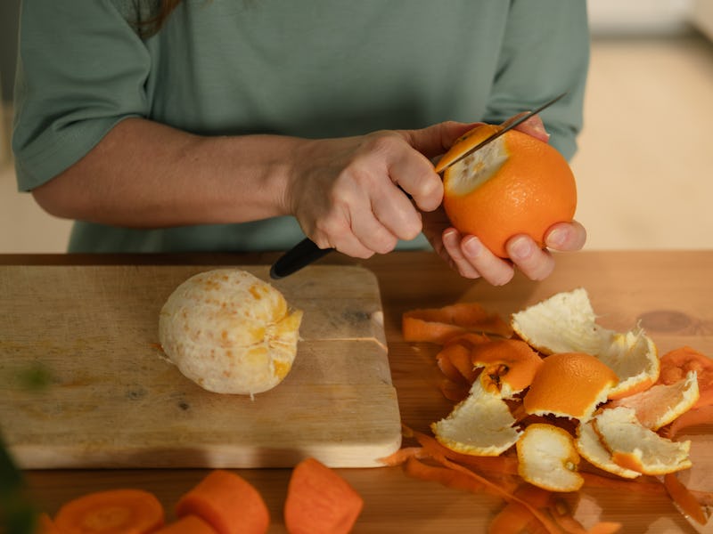 woman peeling an orange at the kitchen table at home. Hands close up