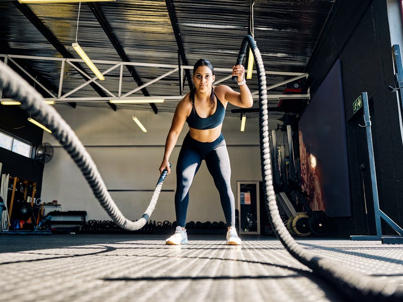 Female athlete performing battle rope exercise in a gym. Front view of a woman doing functional trai...