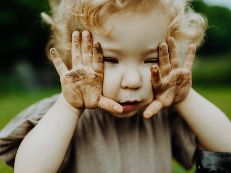 Girl in the garden, playing, working in soil the middle of a vegetable patch. Dirty hands. Sustainab...