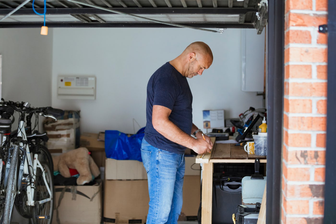 A side-view shot of a male carpenter upcycling, he is measuring a plank of wood on a crafting table, he is wearing casual clothing.