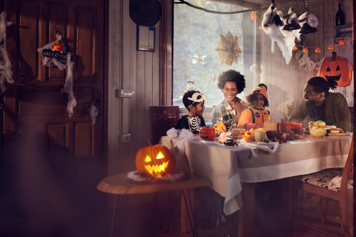 Happy African American parents and their kids communicating in dining room on Halloween day.