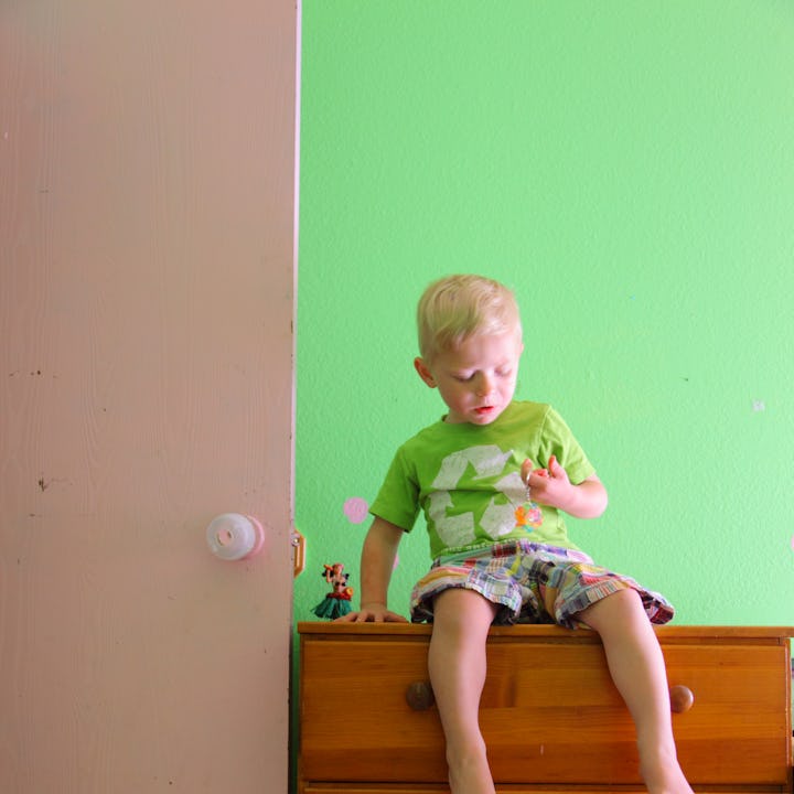 Small child sitting on top of tall bedroom dresser.