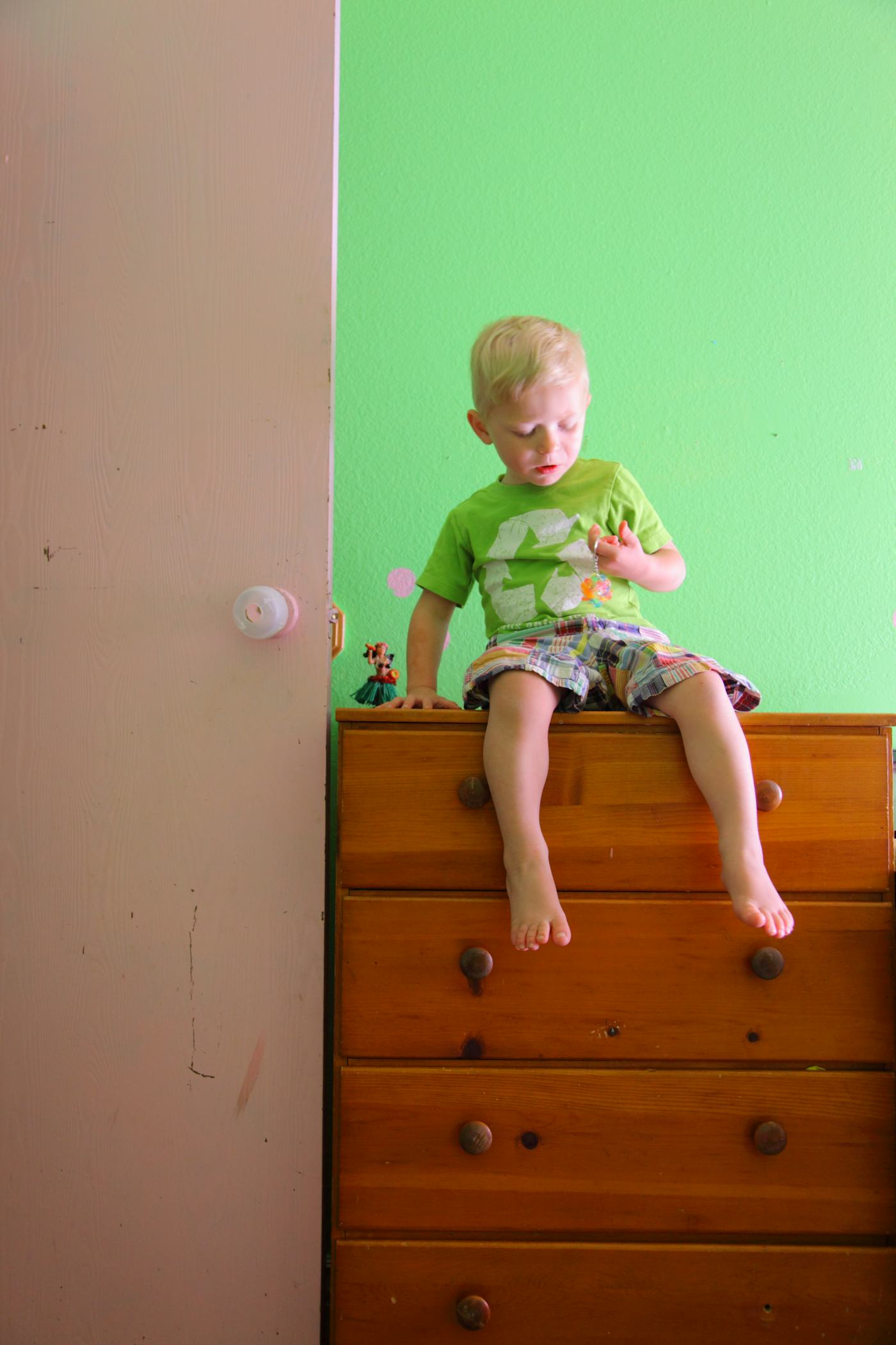 Small child sitting on top of tall bedroom dresser.